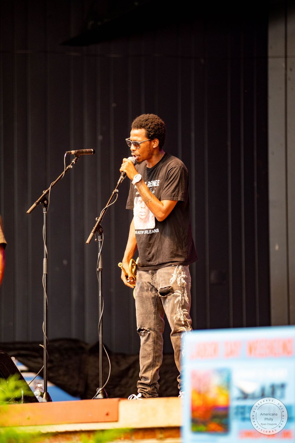 Male vocalist performs on outdoor stage wearing black tee and ripped jeans.
