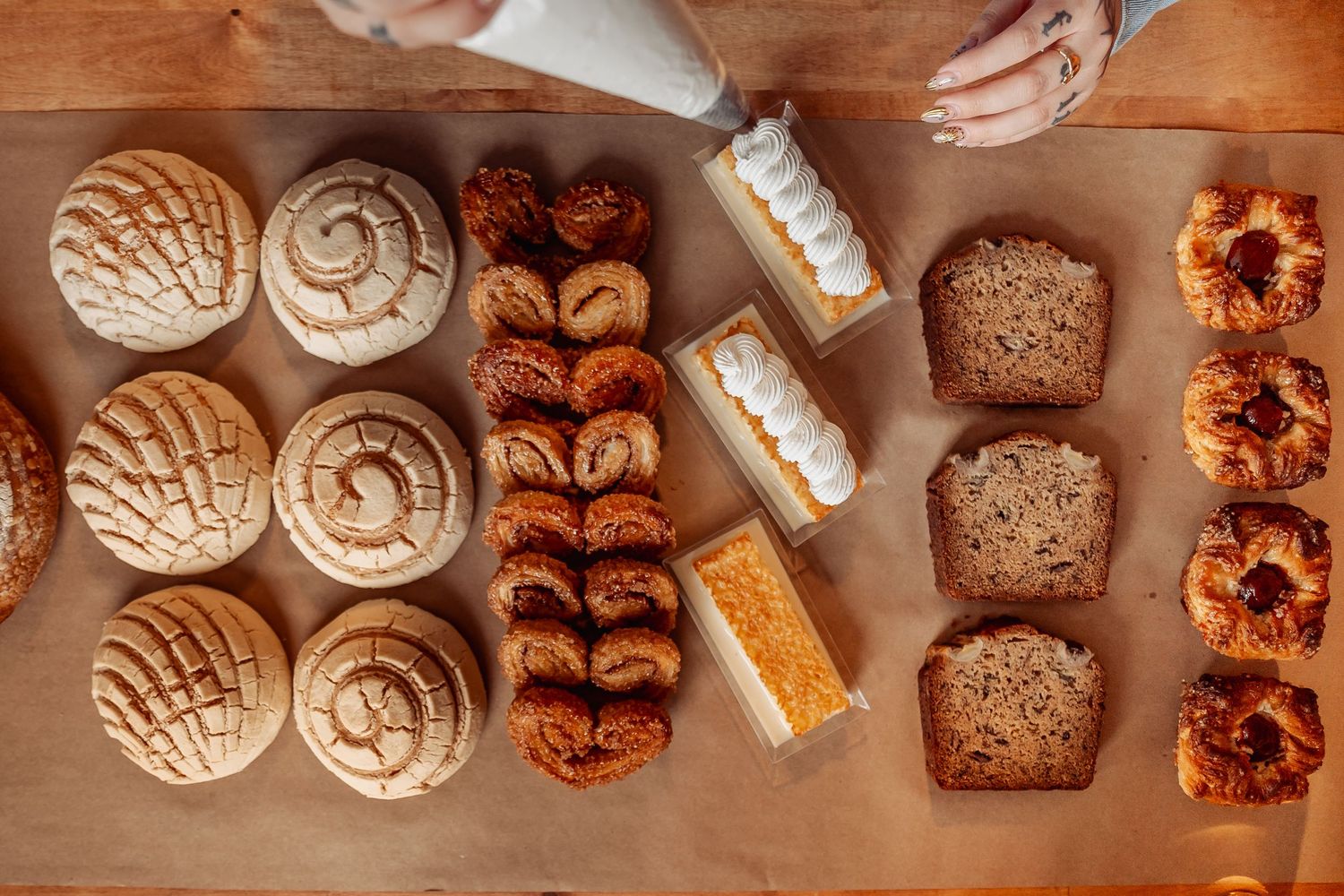 Assorted Mexican pan dulce and pastries arranged on a wooden table, including conchas, sweet breads, and frosted treats.