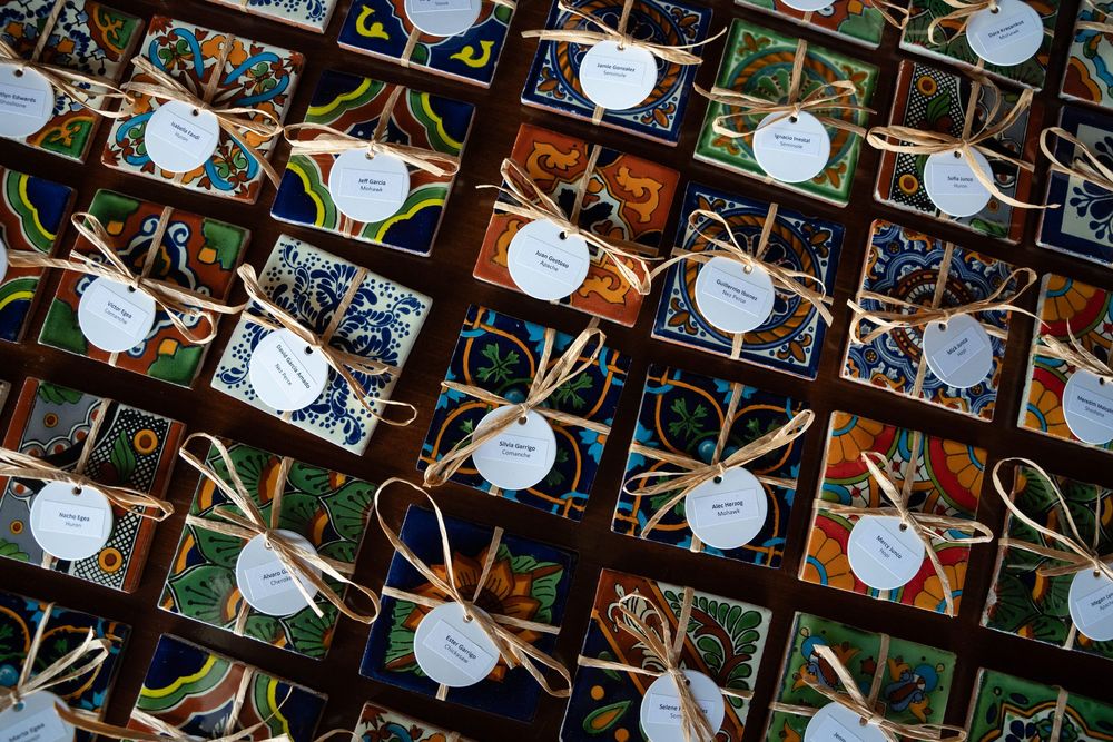 Colorful handmade tile wedding favors tied with twine and white gift tags arranged in rows on a dark surface.
