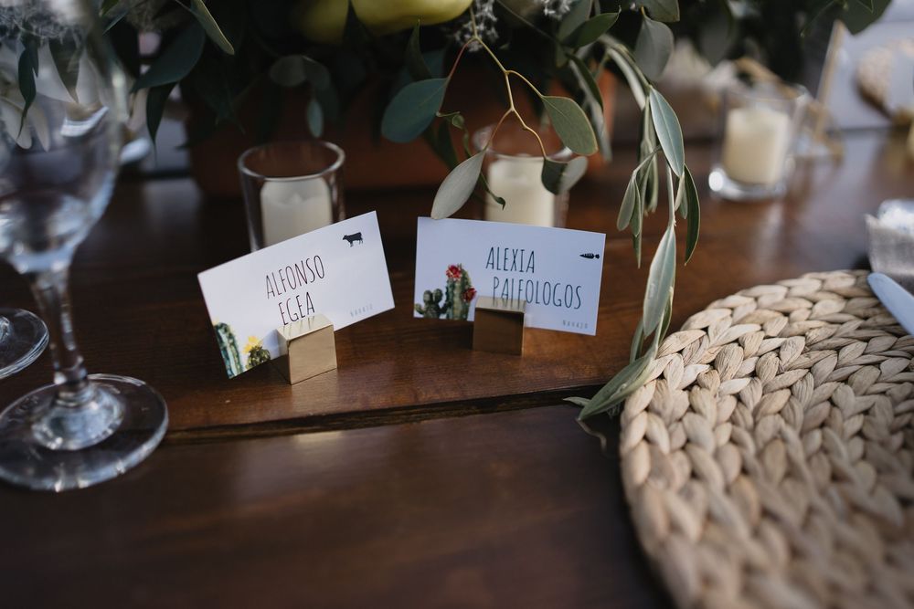 Elegant wedding place cards with cactus designs displayed in wooden holders on a rustic table with greenery.