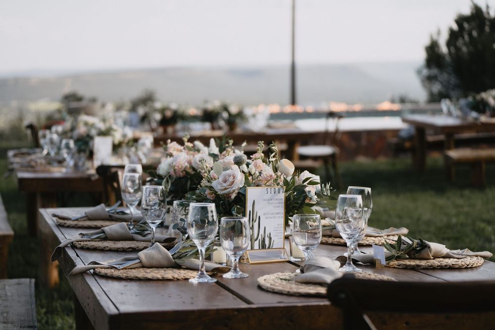 Elegant outdoor wedding reception with rustic wood tables, white floral centerpieces, and glassware set against a scenic landscape.