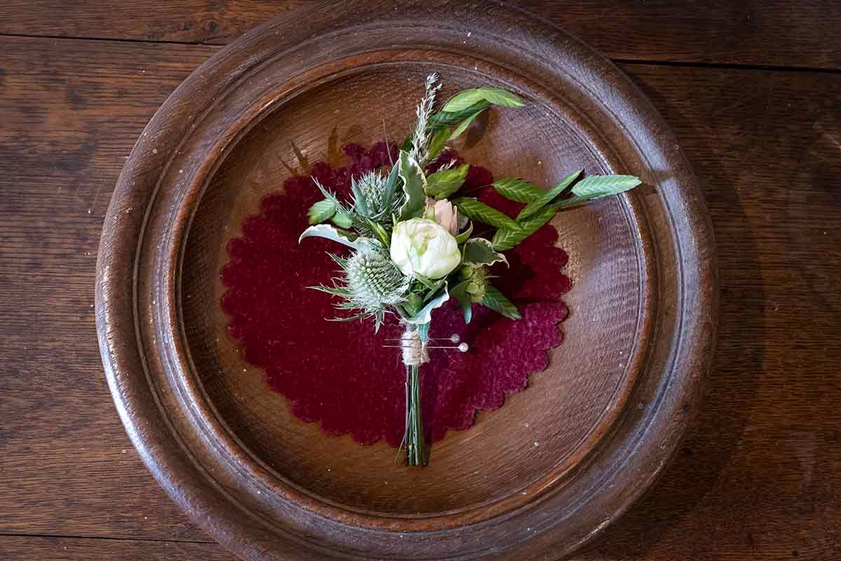 Elegant boutonniere with white rose and thistle on red doily atop rustic wooden plate.
