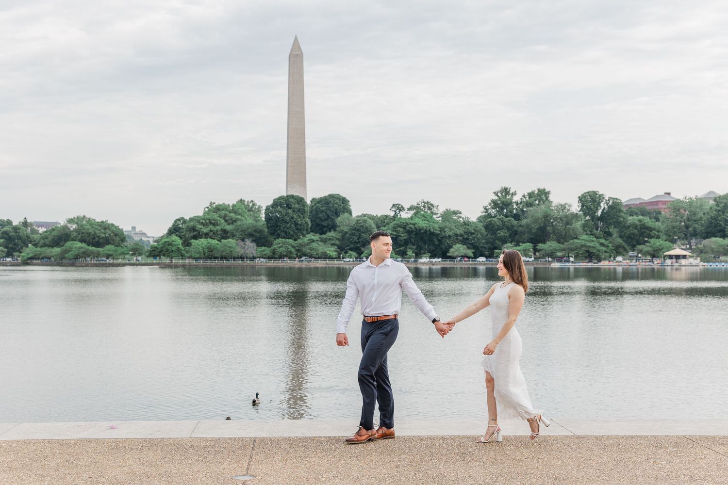 Couple holding hands by the Tidal Basin with the Washington Monument in the background on a cloudy day.