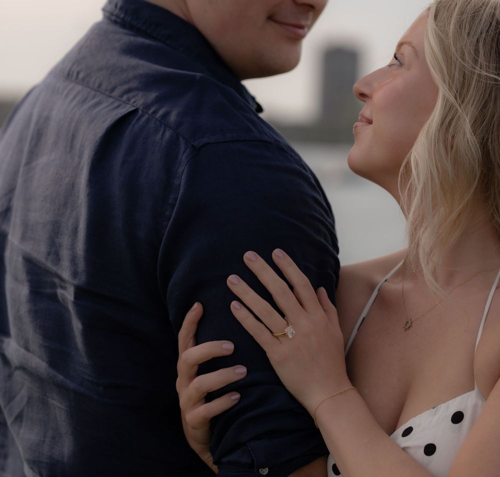 Couple sharing a romantic moment outdoors, woman in polka dot dress gazing up at man in navy shirt near waterfront.