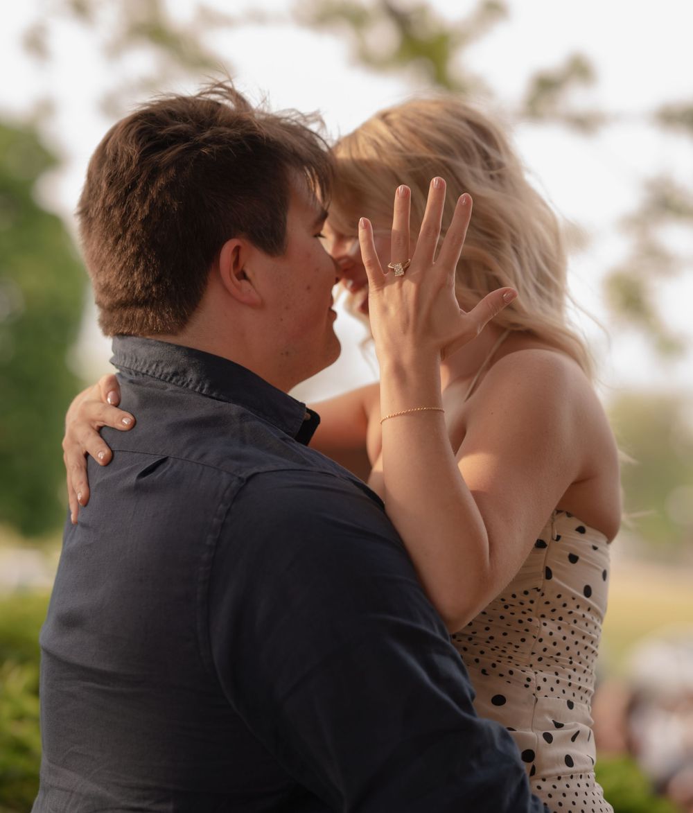 Couple sharing a romantic moment, woman showing off engagement ring while embracing outdoors.