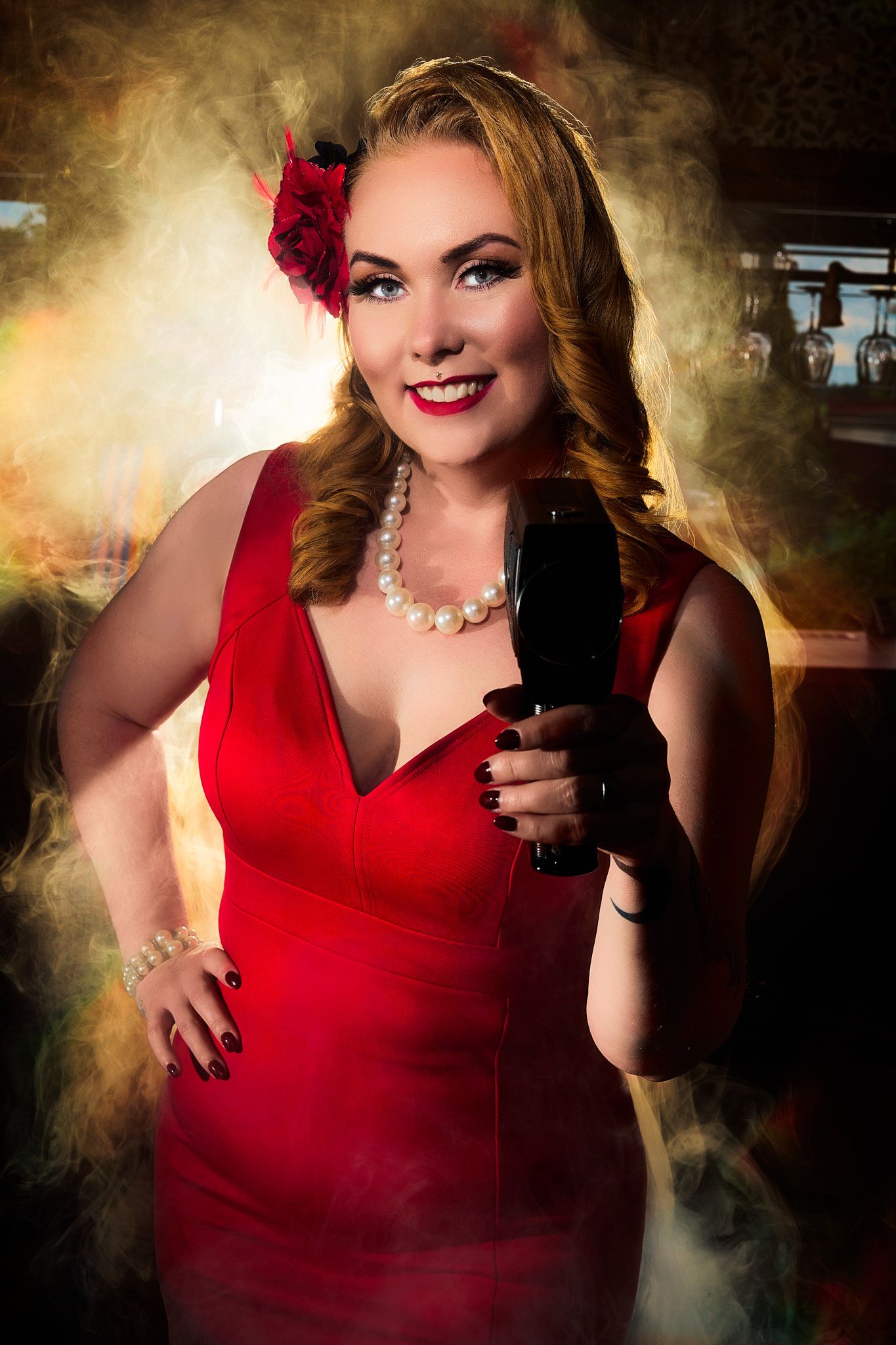 Pin-up woman in a red dress holds a black projector, wearing pearls and a red flower, surrounded by warm golden smoke.
