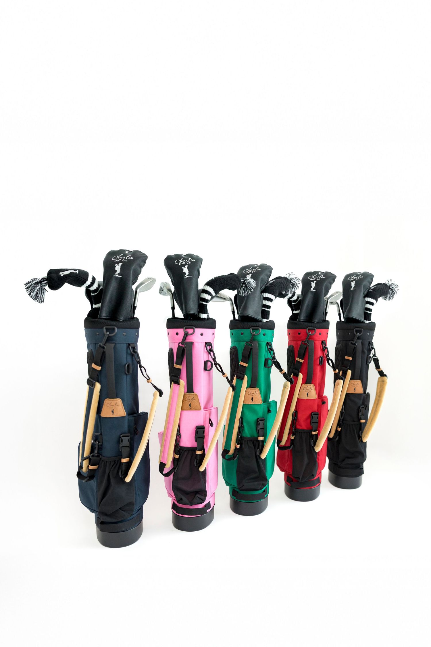 Six colorful junior golf bags in navy, pink, green, and red with clubs and headcovers on white background.