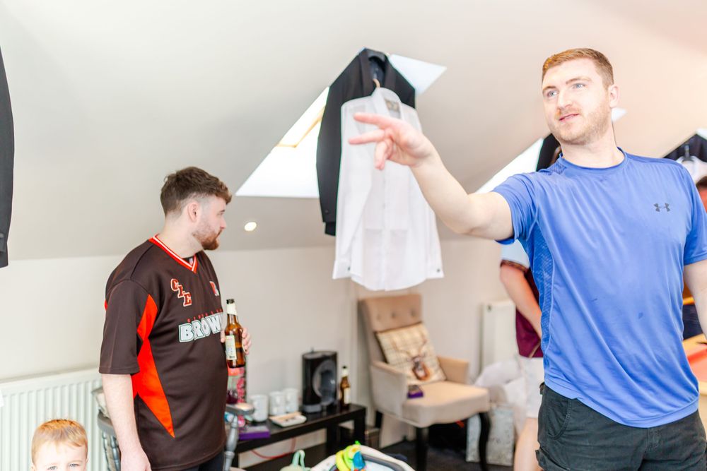 Two young men in a bright room, one holding up a white plastic bag while the other looks on.