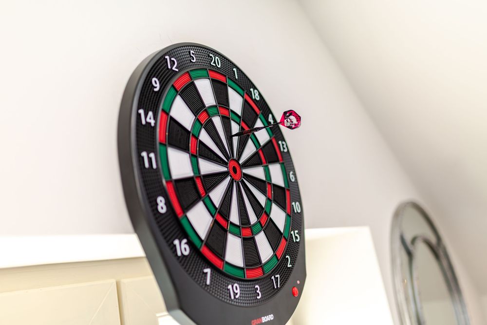 A black dartboard mounted on a white wall with a single red dart hitting near the bullseye center.