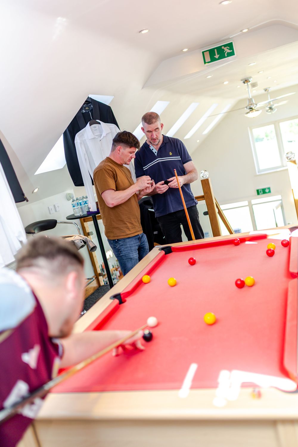 Men playing snooker on a red pool table in a bright attic games room.