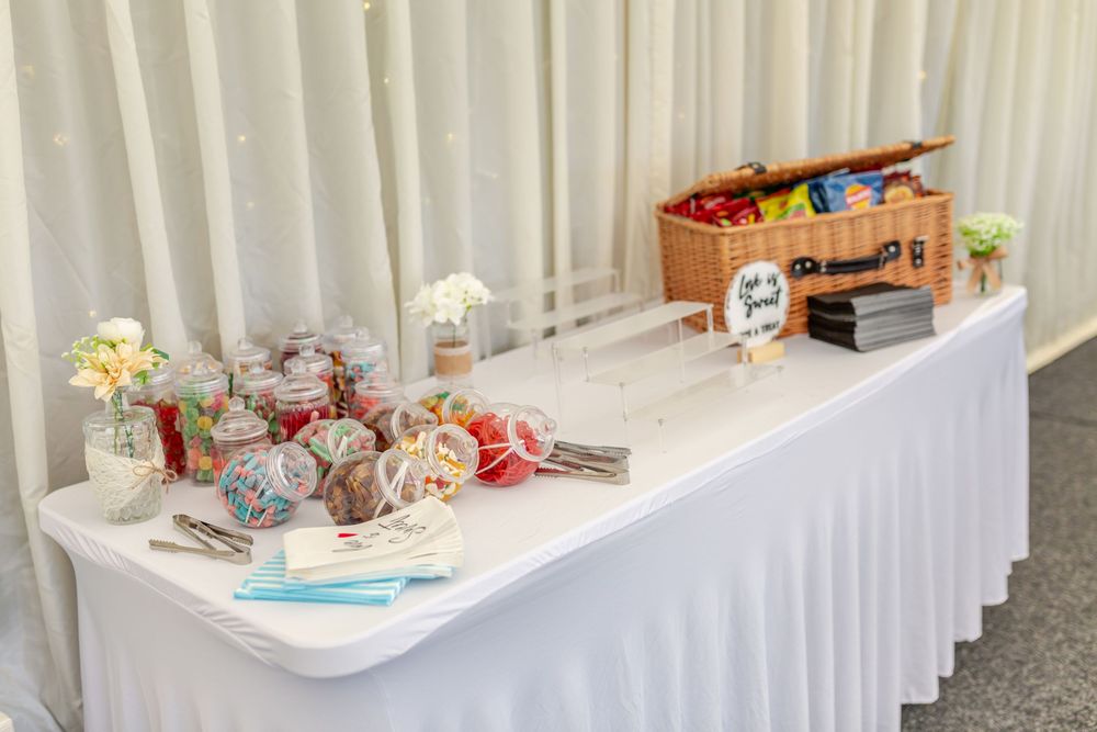 Elegant wedding candy buffet table with white tablecloth, sweets, floral arrangements, and a wicker basket display.