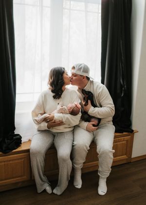 Parents sitting together and holding their newborn baby near a window during an in-home newborn session