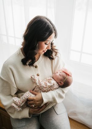 Mother gently holding her newborn baby near a window during an in-home newborn session