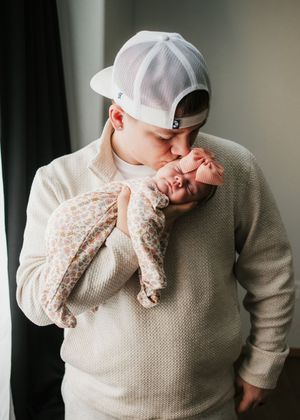 Father wearing a knit hat and gently holding his newborn baby close to his face