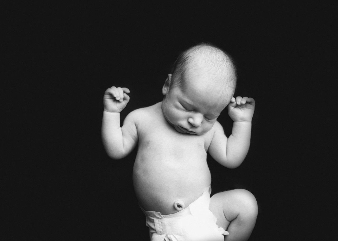 Black and white portrait of a newborn baby lying on their back with arms raised