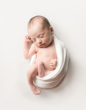 Sleeping newborn baby curled up in a white wrap on a light background