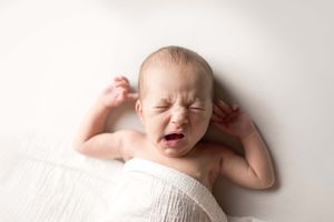 Newborn baby lying on a white blanket with eyes closed and mouth open in a sleepy expression