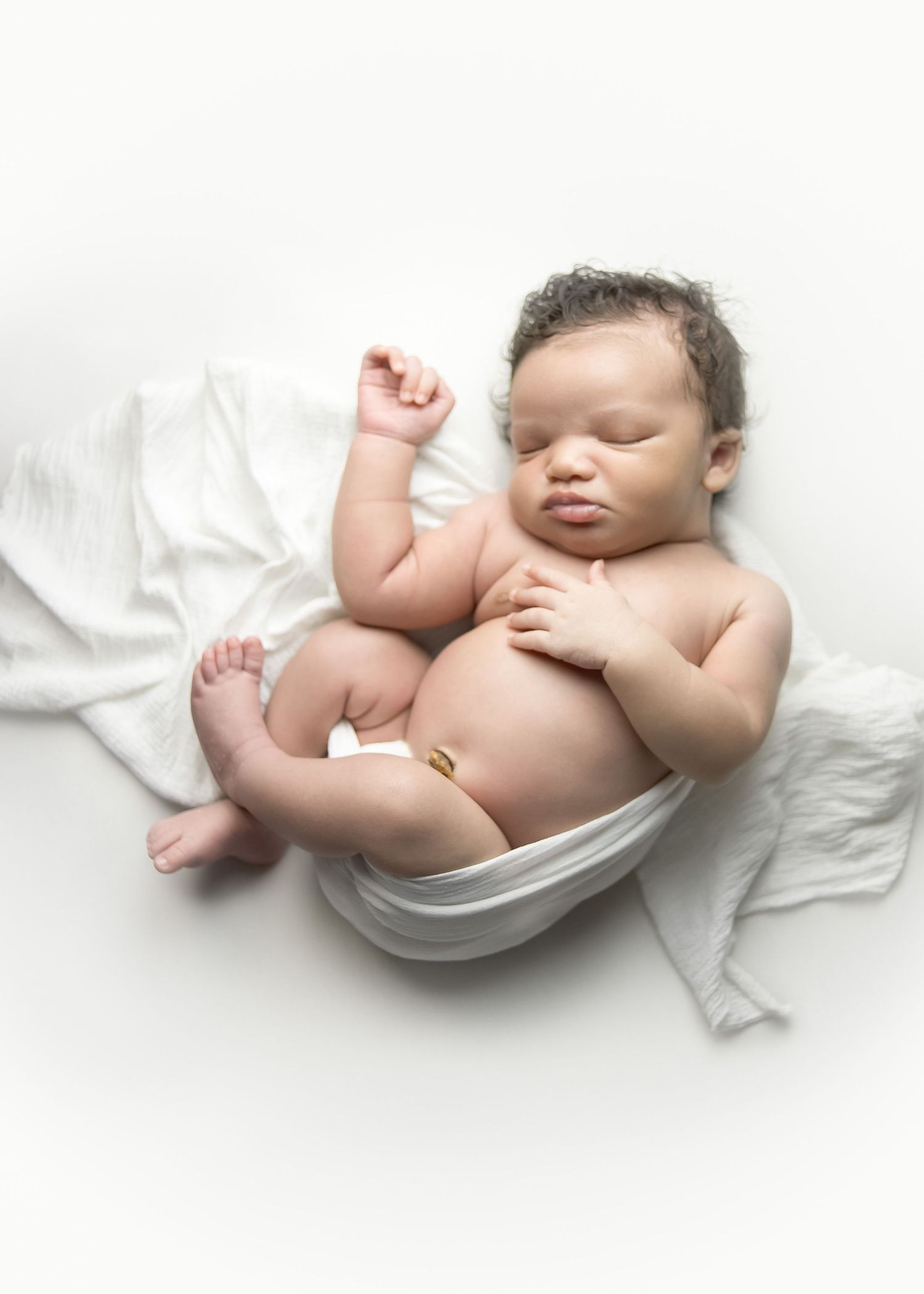 Newborn baby lying on a white blanket with arms and legs curled up