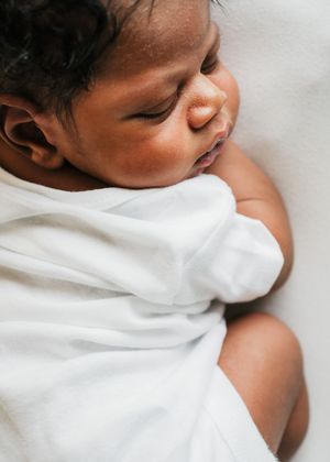 Newborn baby wrapped in a white blanket and resting peacefully on their side