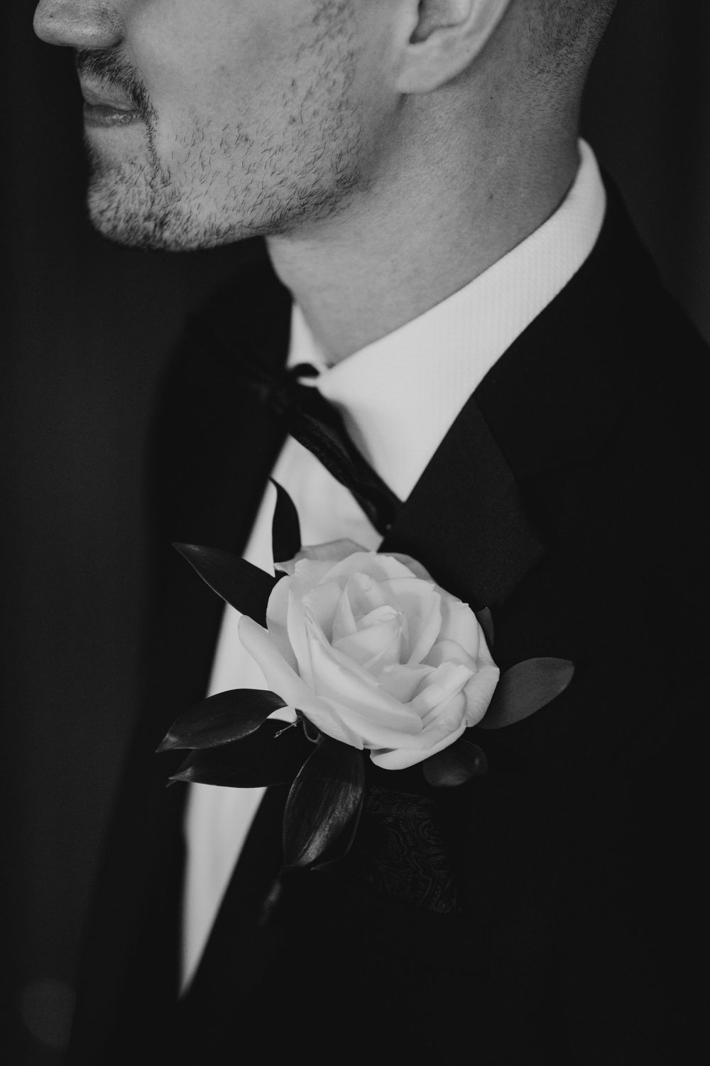 Black and white photo of a groom in a tuxedo with a white rose boutonniere and bow tie.