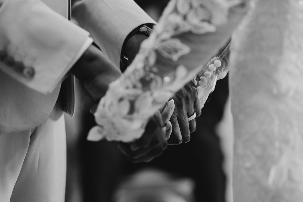 Black and white wedding photo of bride and groom holding hands, with floral bouquet visible.