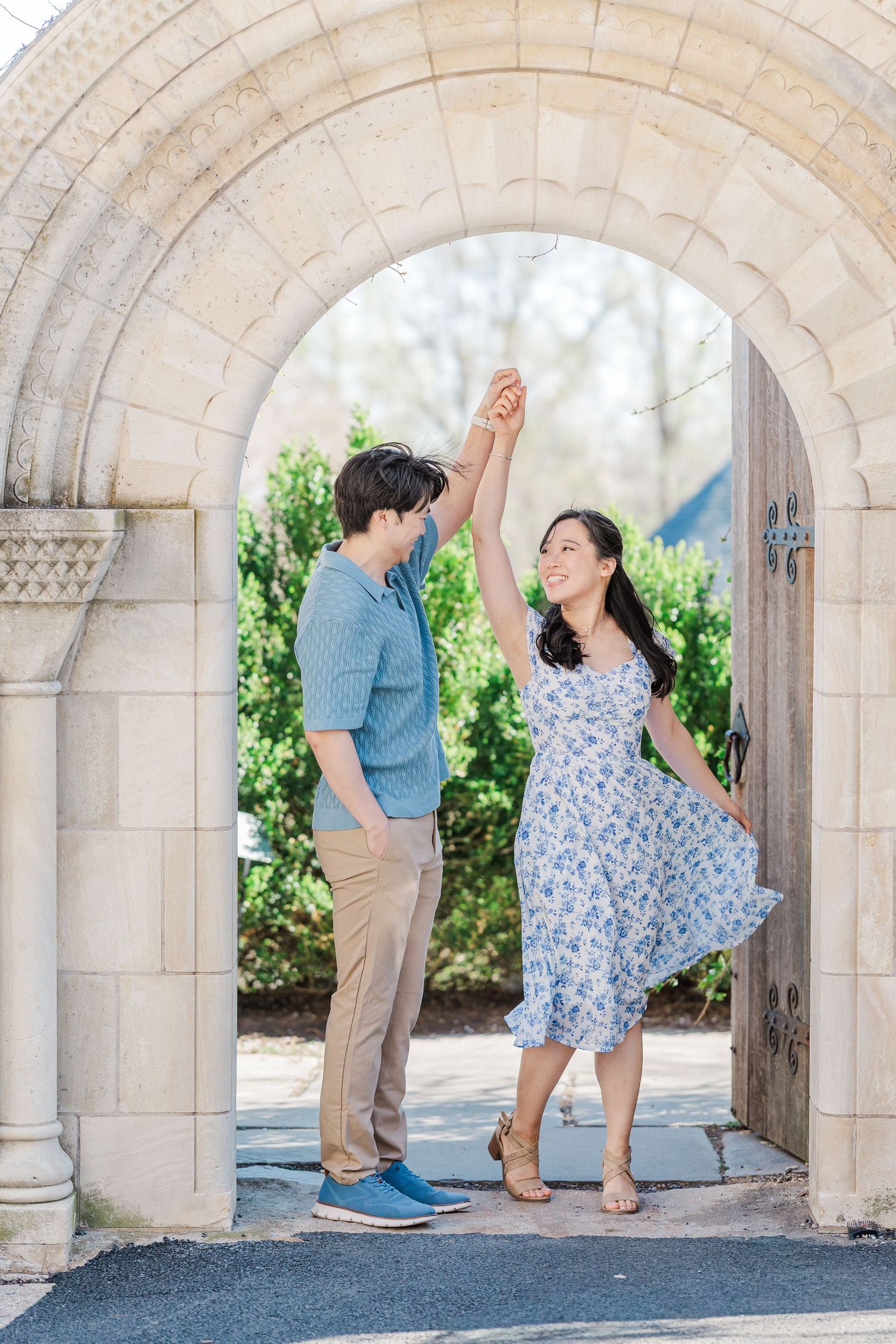 Couple dancing under a stone arch doorway, man in blue shirt spinning woman in floral dress outdoors.