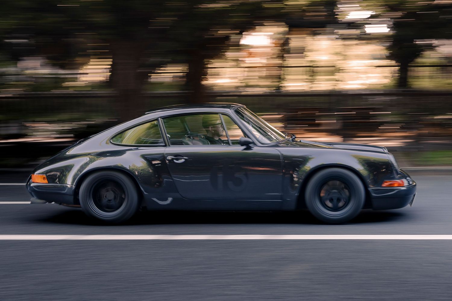 A dark grey Porsche 911 speeding along a road with motion-blurred background trees.