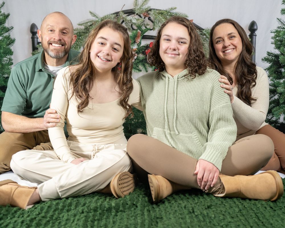 Family of four smiling together in front of Christmas trees during a festive holiday photo session.