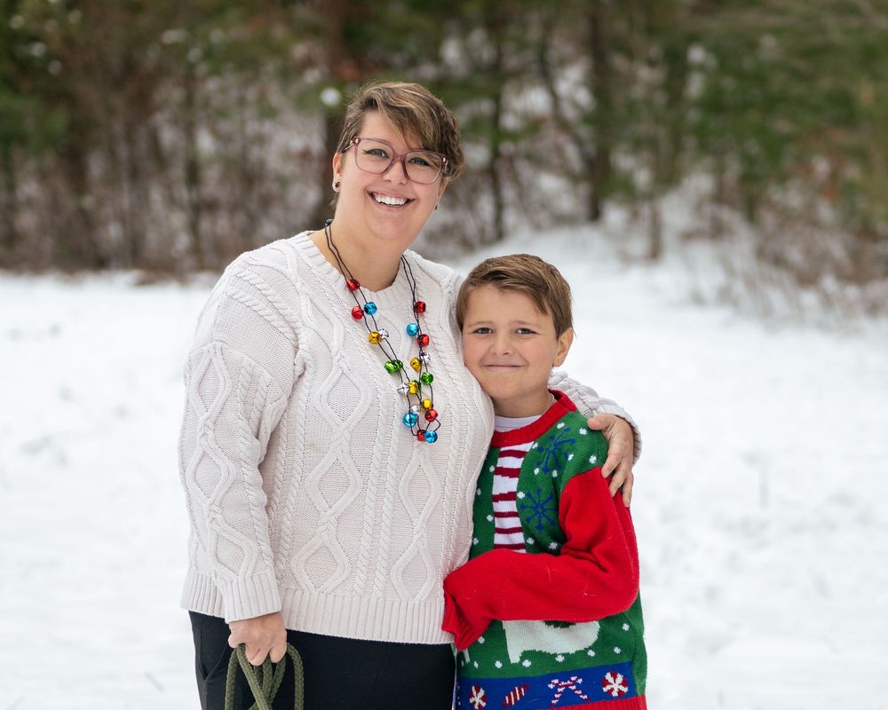 Woman and boy in Christmas sweaters smiling together in snowy winter outdoor setting.