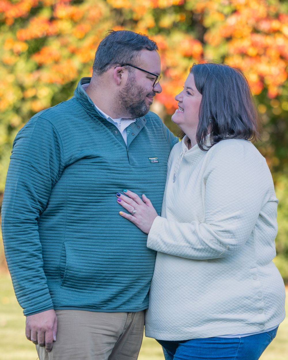 Couple sharing a romantic moment outdoors in autumn, wearing casual sweaters with colorful fall foliage behind them.