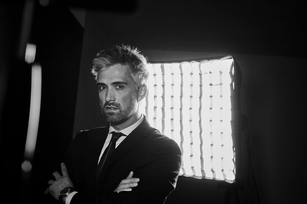 Black and white portrait of a businessman with arms crossed posing in front of a studio light.