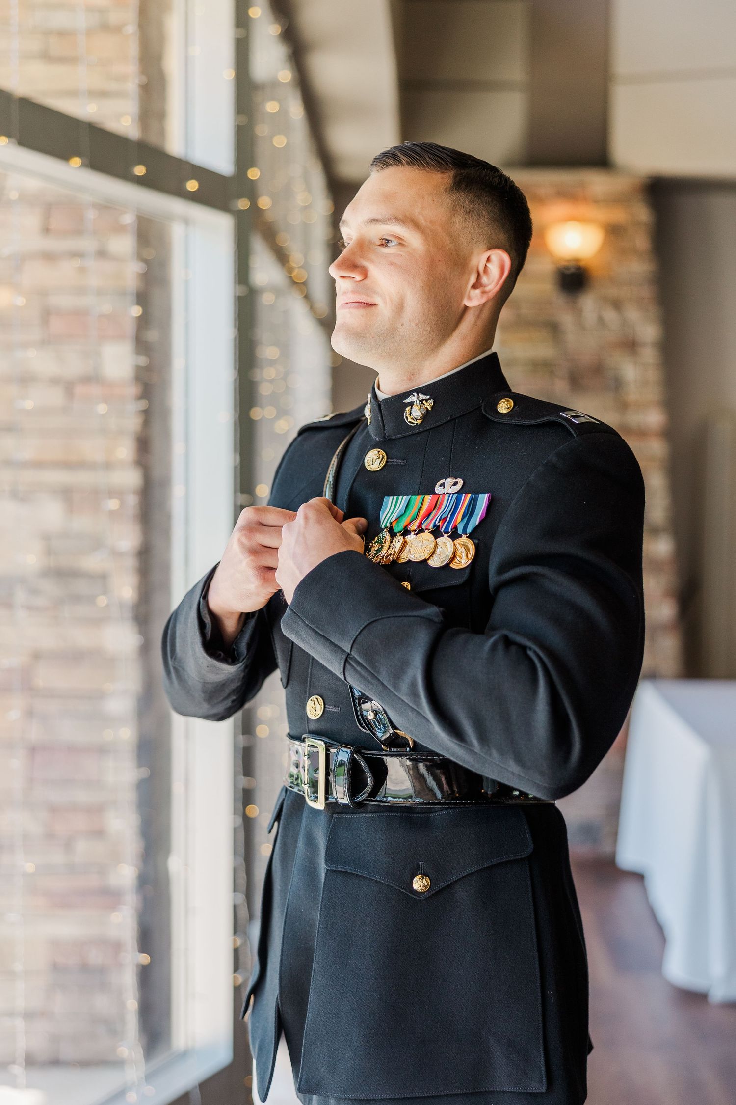 Marine in dress blues uniform with medals smiling by window in elegant venue.