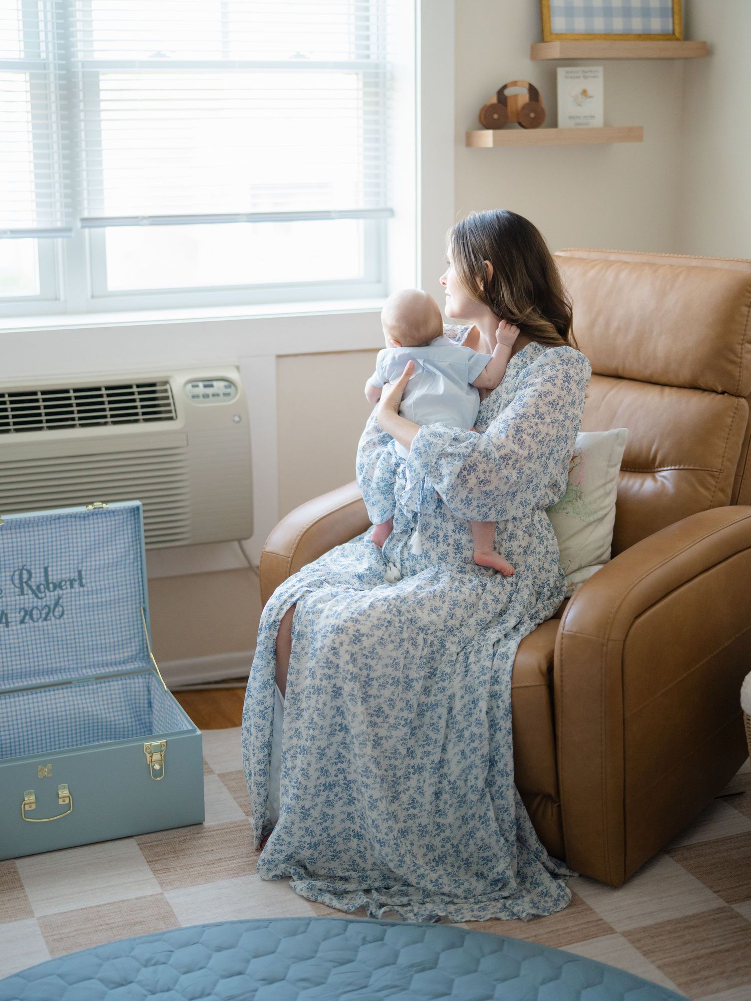 Young mother holds her newborn in her arms while sitting in his nursery chair.