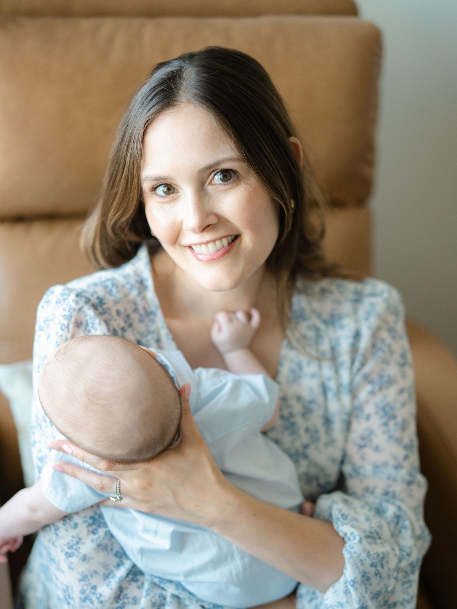 Close up of mother's face wearing a blue floral dress holding her newborn boy.