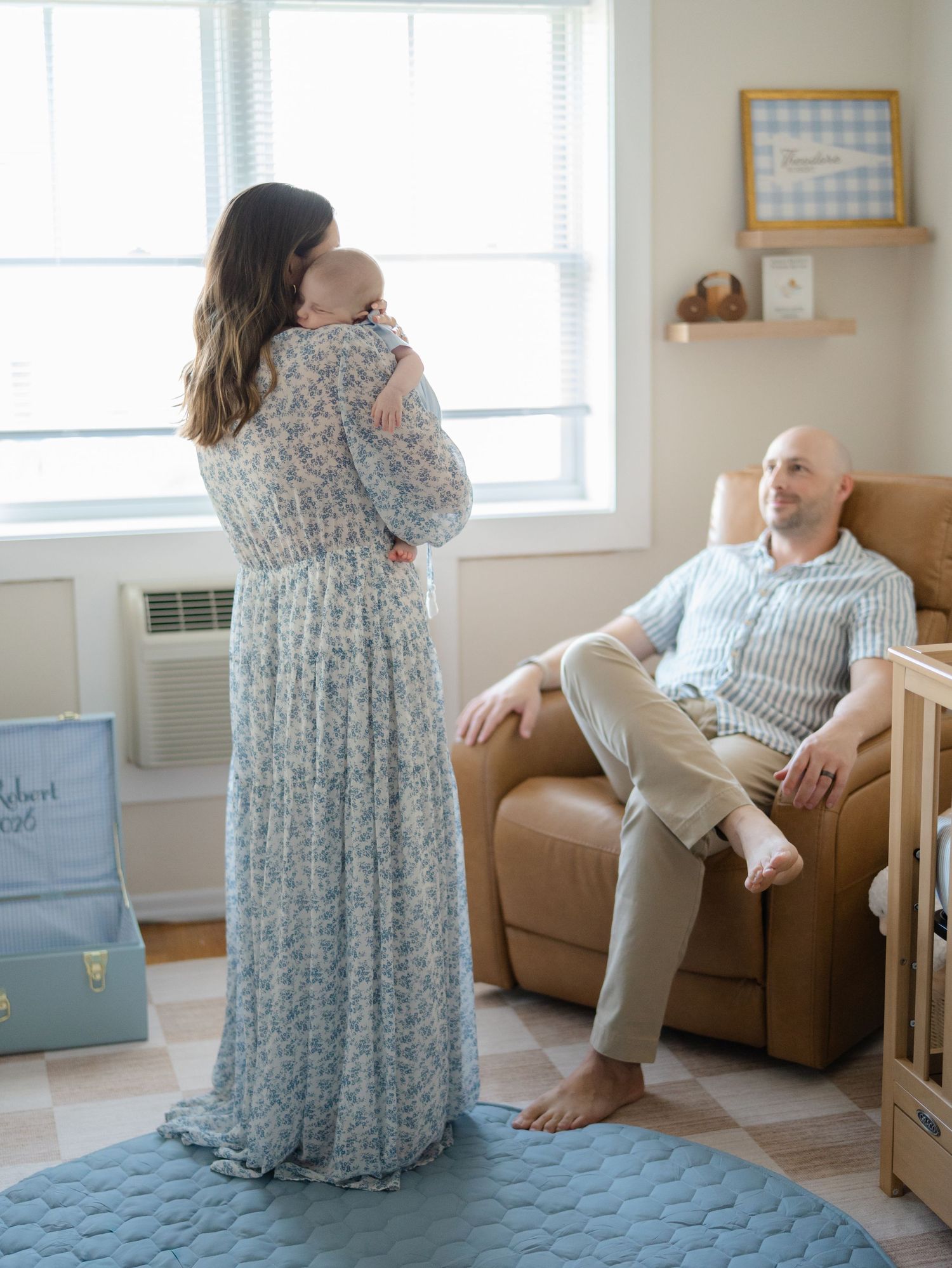 White and neutral coastal baby nursery in Belmar, NJ featuring natural woven accents with parents standing smiling at each other.