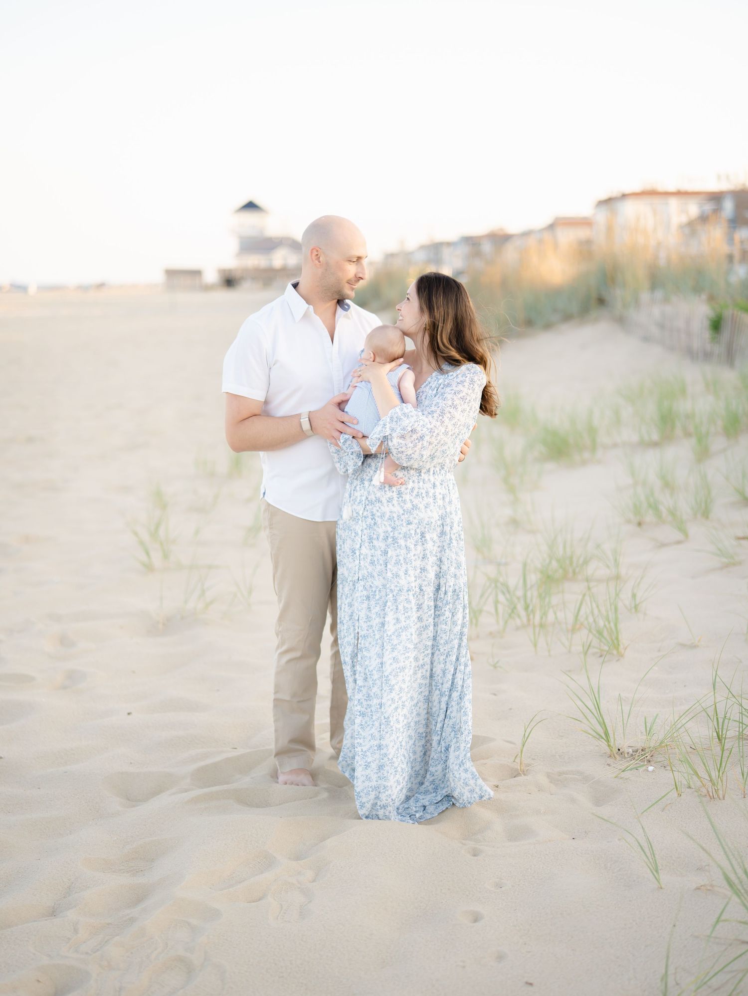Parents hold newborn baby barefoot along the dunes at Belmar Beach NJ.
