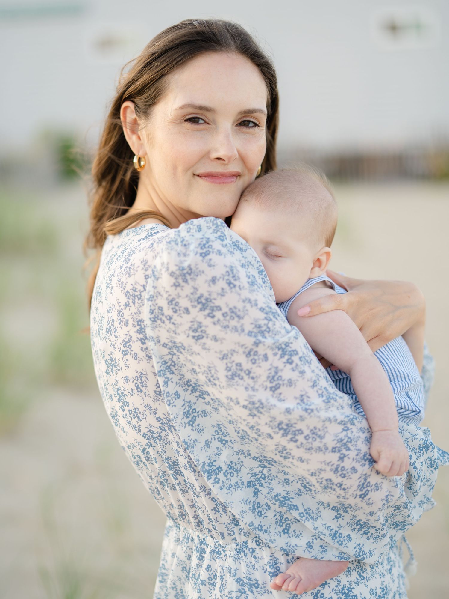 Mom wearing flowy linen dress cuddling baby near Belmar beach dunes during golden hour.