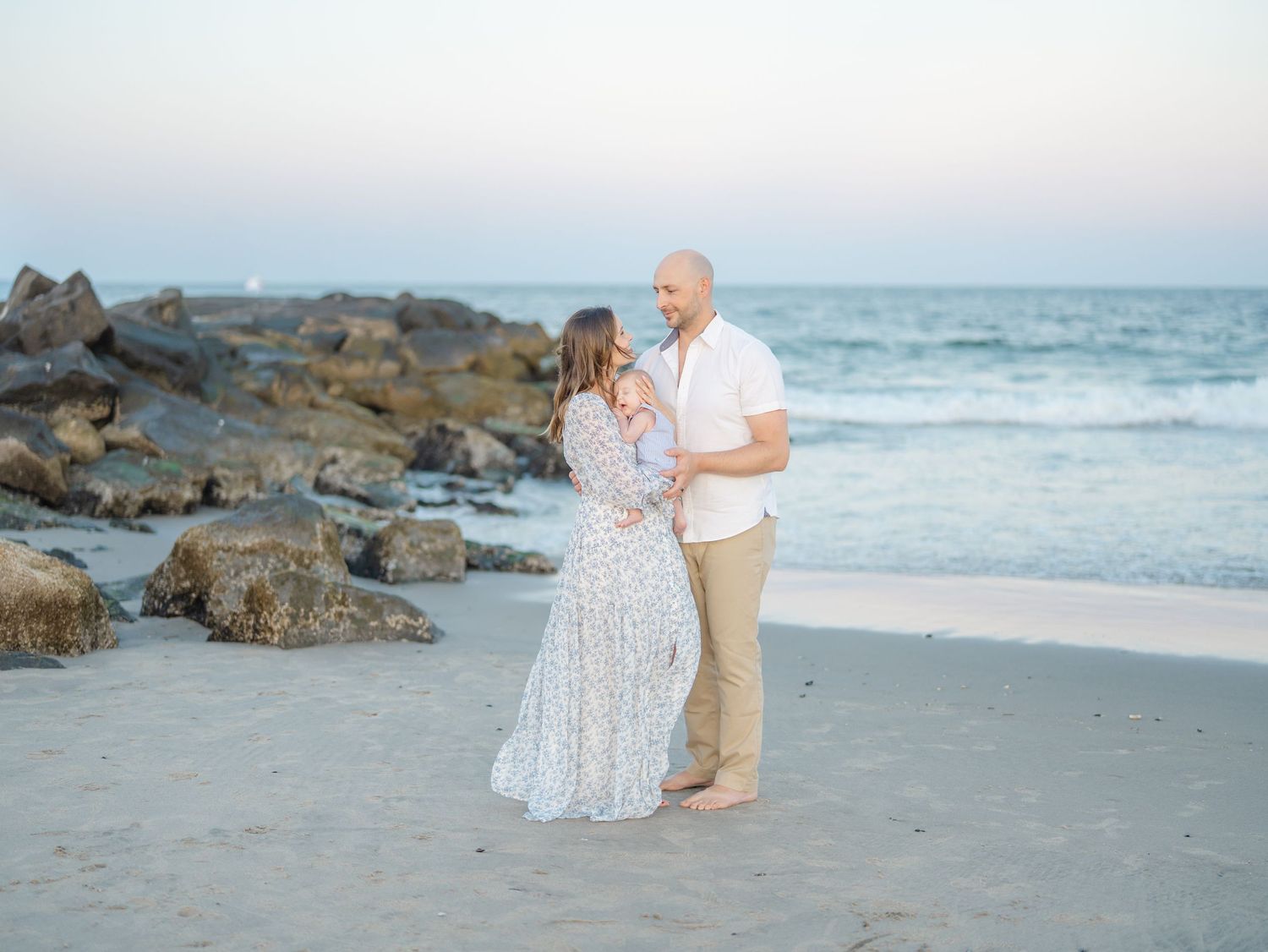 Lauren marie photography capturing parents cuddling baby in front of the ocean in August.