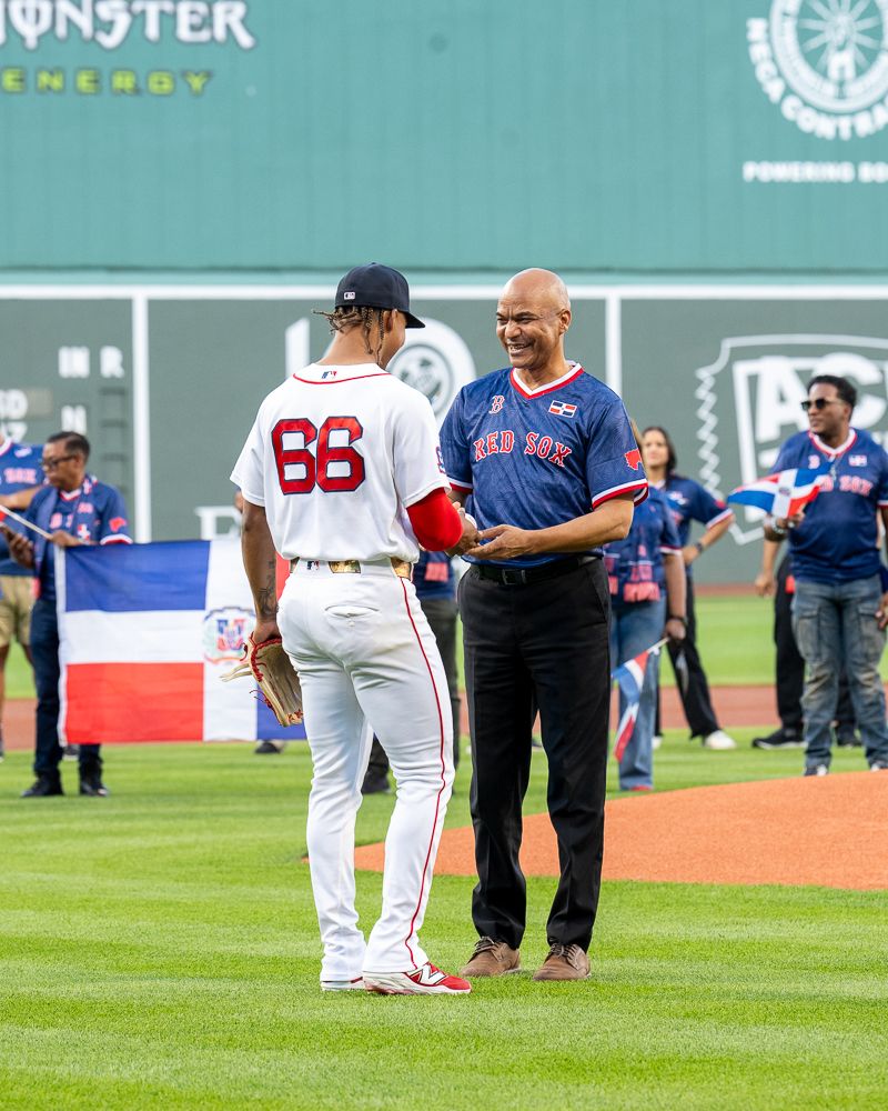 Two Boston Red Sox players shake hands on Fenway Park field during a Dominican Republic celebration event.