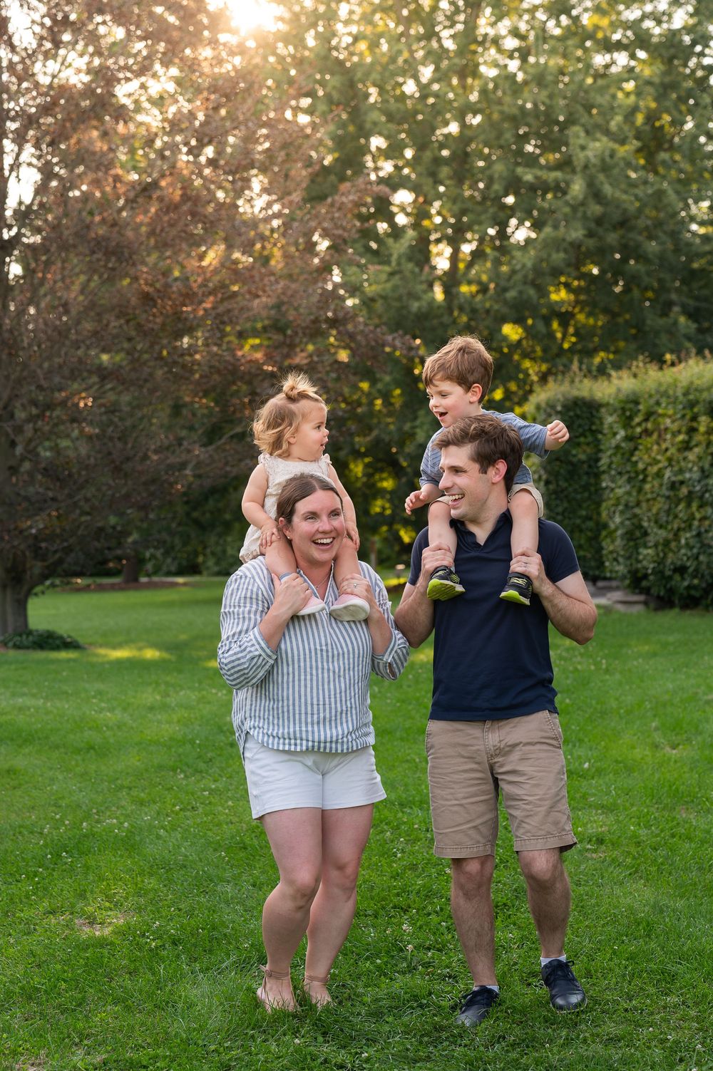 Happy family with two young children on their shoulders enjoying a sunny day in a lush green park.