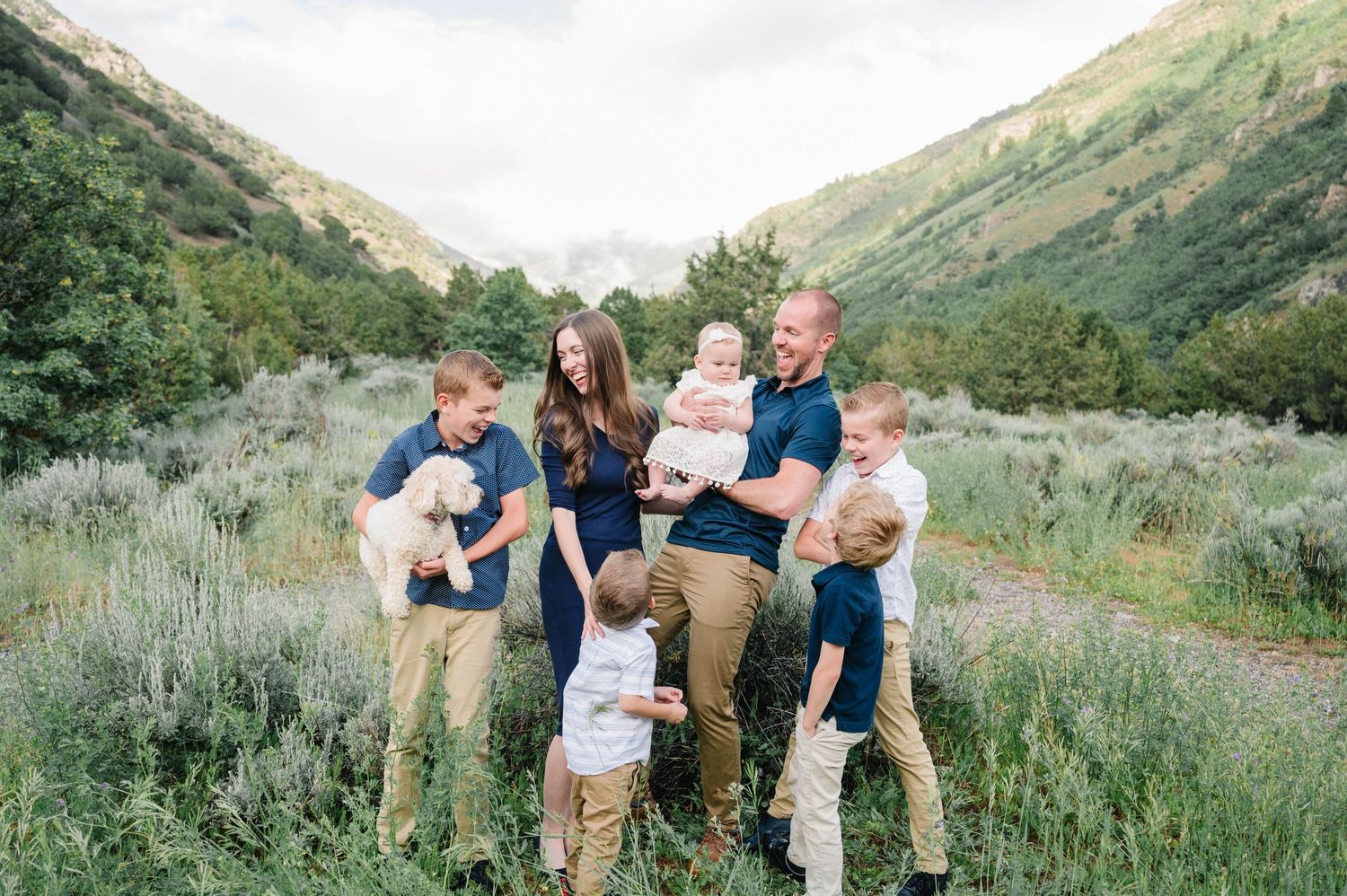Group posing together outdoors in front of mountain scenery with green foliage.