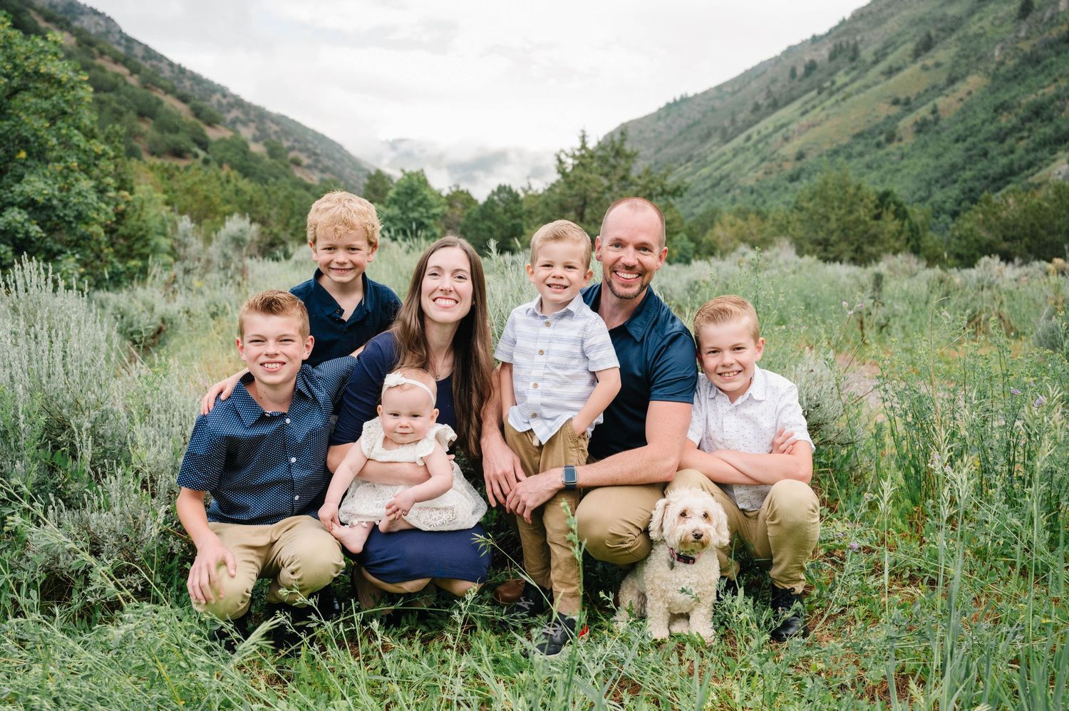 Family and dog posing together in scenic mountain valley with sage brush.