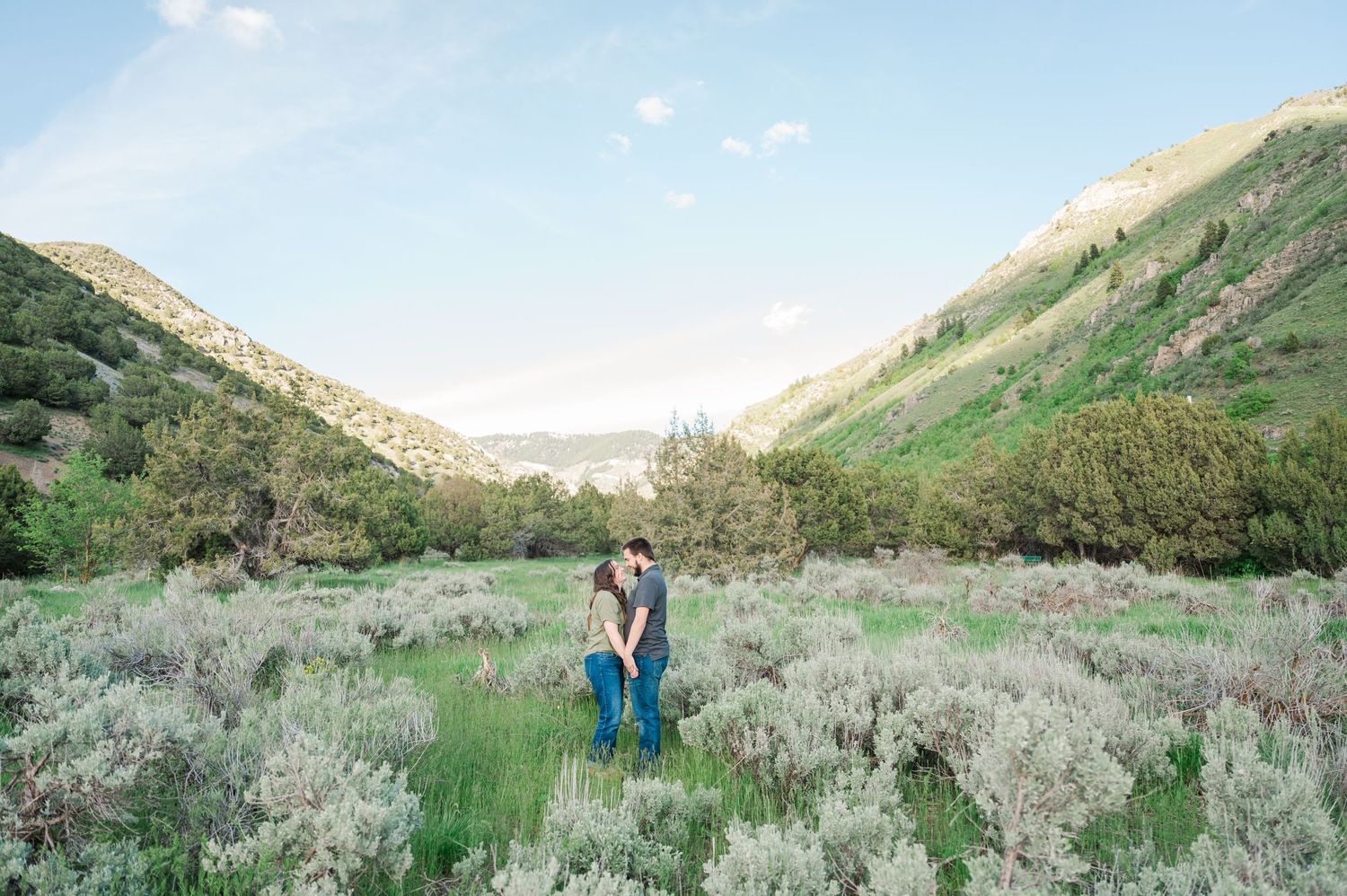 A couple stands together in a scenic mountain valley surrounded by spring wildflowers.