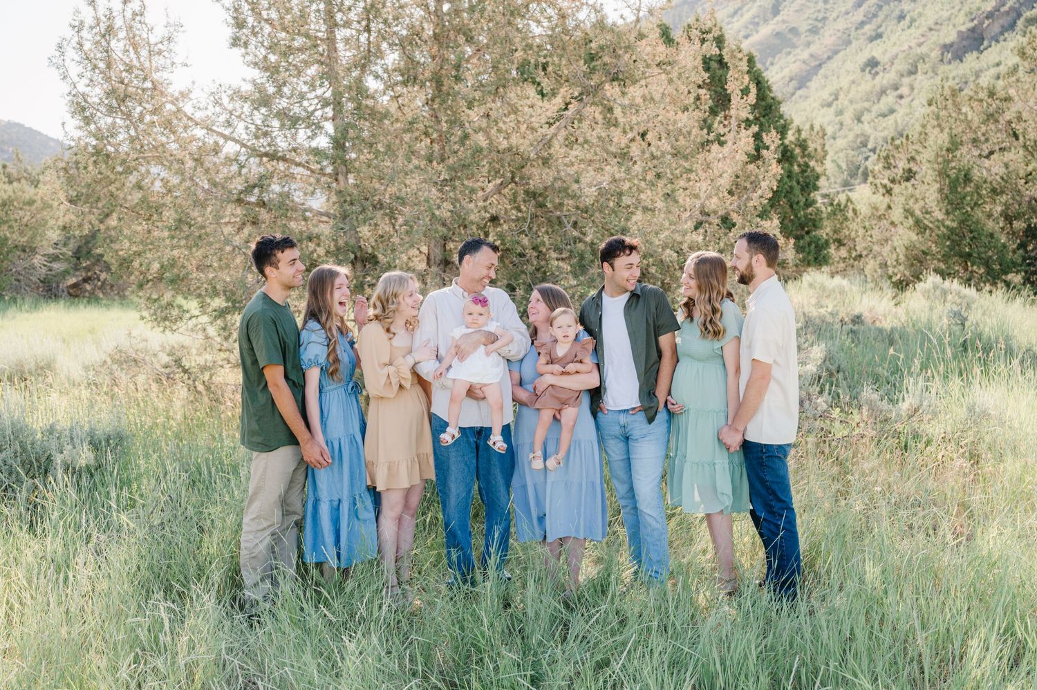 Group portrait of family members in casual attire standing together in a grassy field with mountains in background.