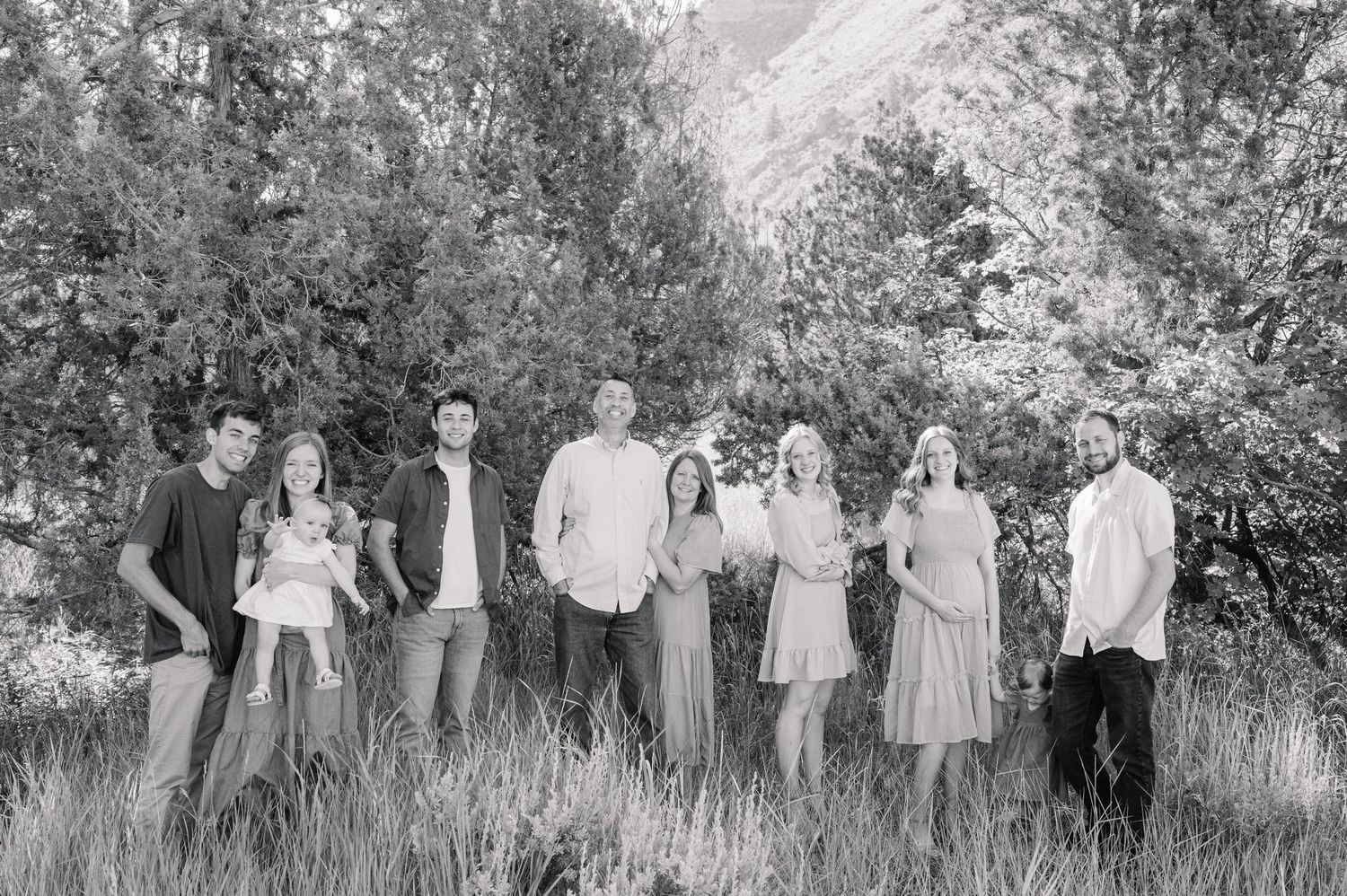Black and white photo of group standing together in tall grass with trees and mountainside behind them.