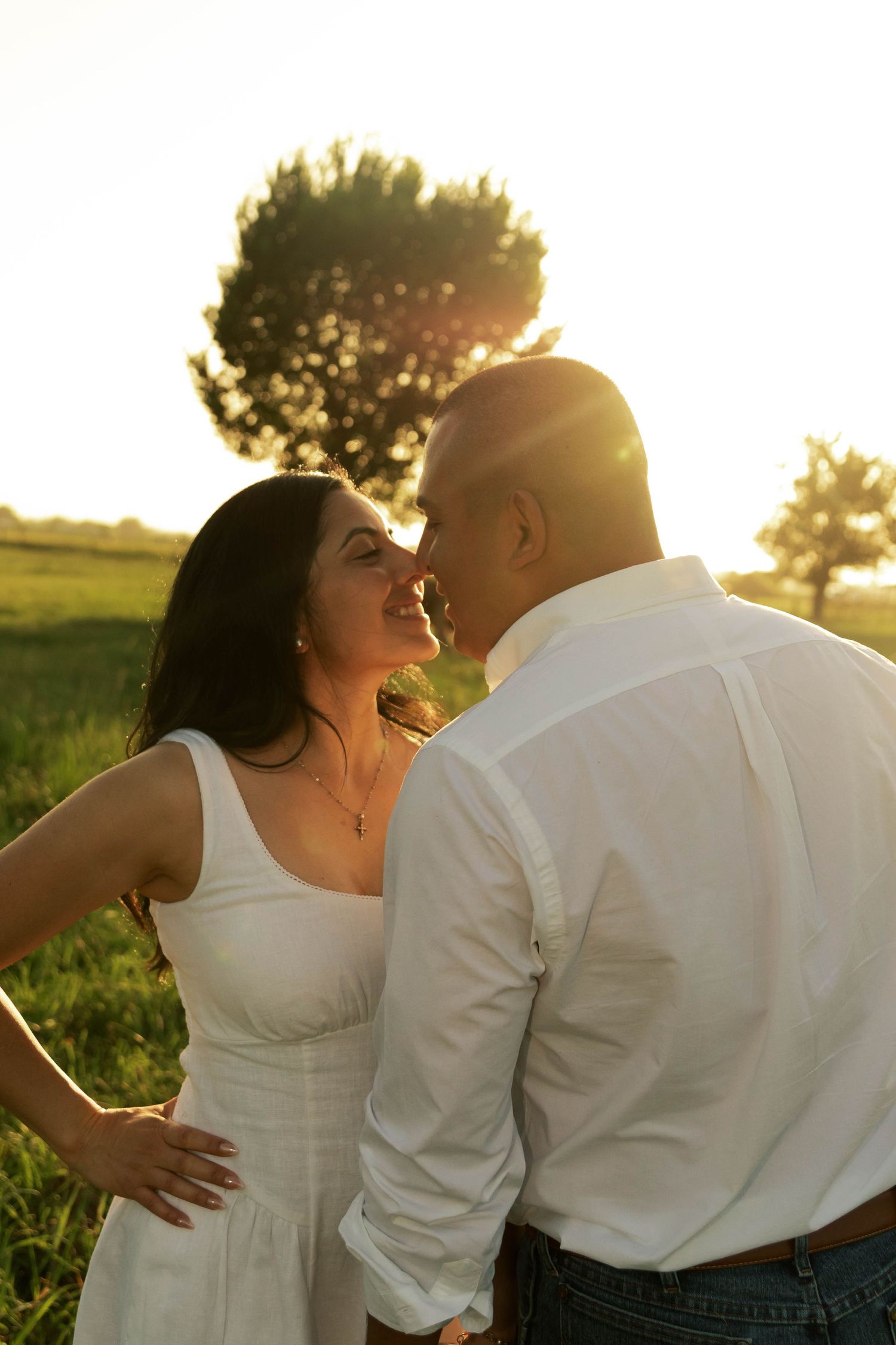 Couple sharing a romantic moment at golden hour sunset in a green field.