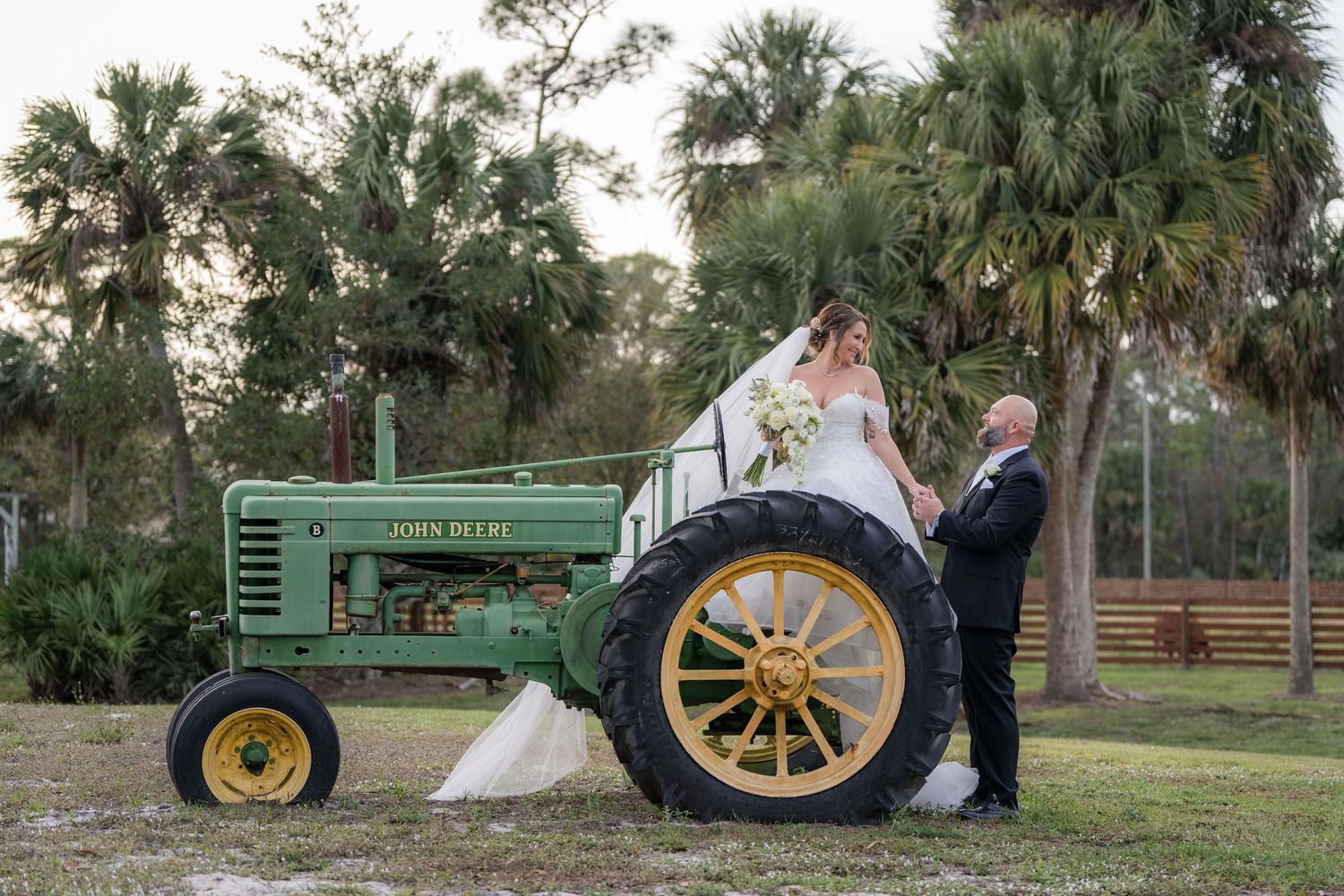 Bride sitting on a vintage green tractor with her groom during portraits at Rockin' H Ranch in Palm City, FL