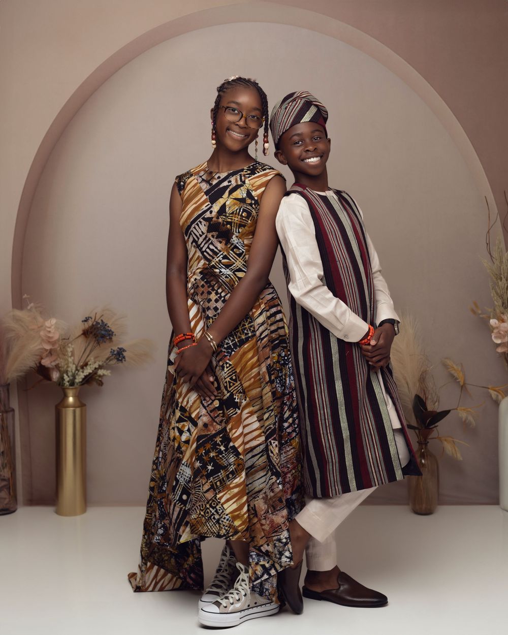 Two people in vibrant African print attire pose together against an arched studio backdrop.