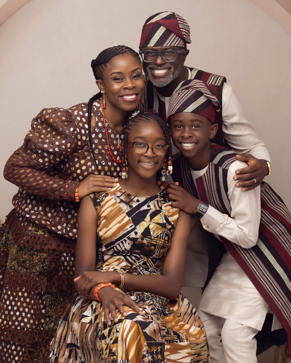 A joyful African family of four in colorful traditional attire posing together for a portrait photo.