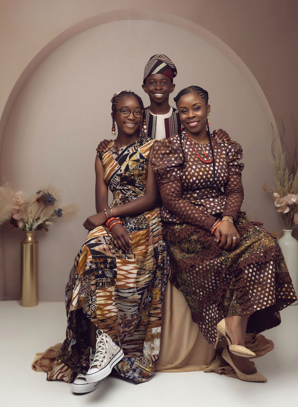 Three people in vibrant African print outfits pose together for a professional studio portrait photo.